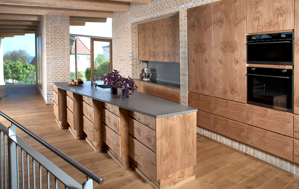 Mittelgroße Nordische Küche mit flächenbündigen Schrankfronten, hellbraunen Holzschränken, Küchenrückwand in Grau und Kücheninsel in Aalborg