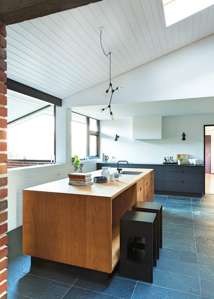 Immagine di un grande cucina con isola centrale industriale con ante lisce, top in legno e pavimento grigio
