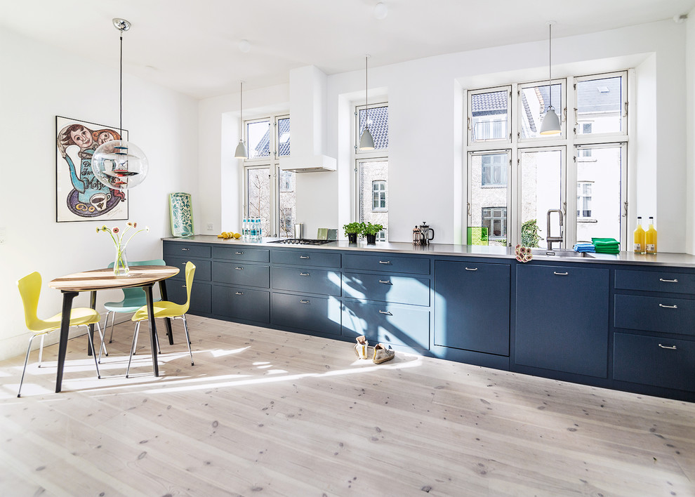 コペンハーゲンにある北欧スタイルのおしゃれなキッチン (一体型シンク、フラットパネル扉のキャビネット、青いキャビネット、ステンレスカウンター、パネルと同色の調理設備、淡色無垢フローリング、アイランドなし、ベージュの床) の写真