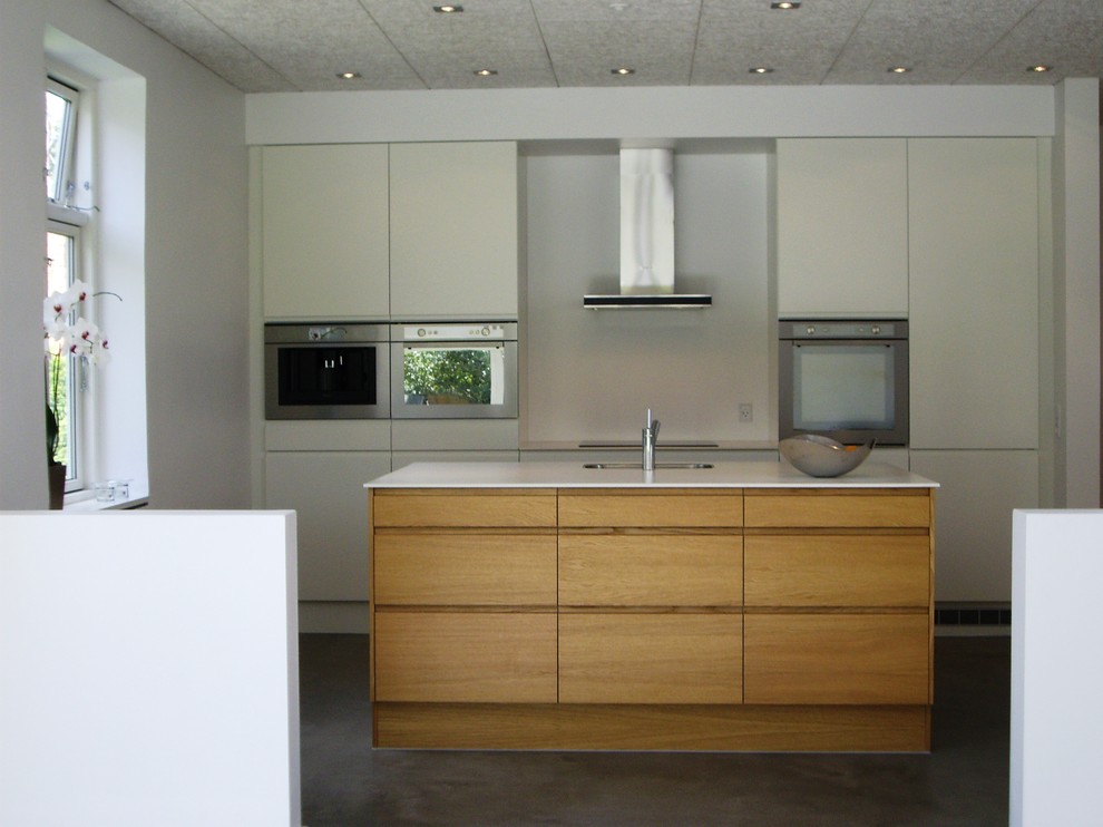 Bild på ett mellanstort nordiskt vit linjärt vitt kök med öppen planlösning, med en undermonterad diskho, släta luckor, bänkskiva i kvarts, vitt stänkskydd, glaspanel som stänkskydd, rostfria vitvaror och en köksö