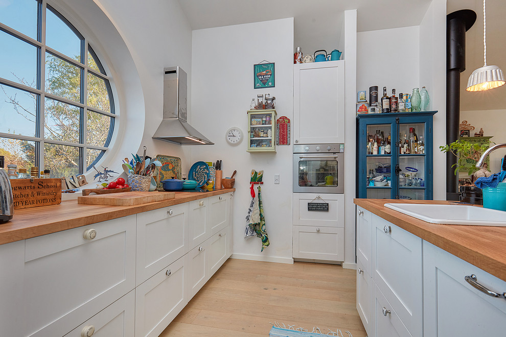 Photo of a bohemian l-shaped kitchen in Copenhagen with a built-in sink, shaker cabinets, white cabinets, wood worktops, stainless steel appliances, light hardwood flooring, beige floors and brown worktops.