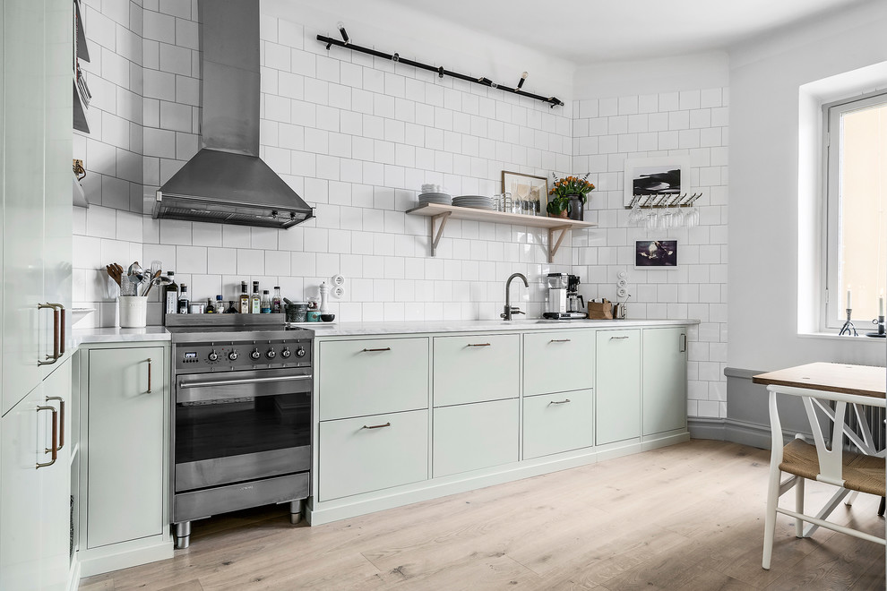 コペンハーゲンにある北欧スタイルのおしゃれなダイニングキッチン (フラットパネル扉のキャビネット、白いキッチンパネル、シルバーの調理設備、淡色無垢フローリング、アイランドなし、ベージュの床) の写真