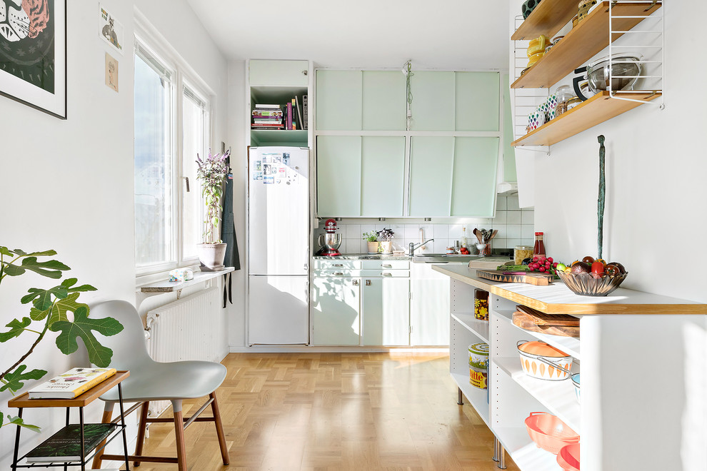 Medium sized scandinavian galley kitchen in Copenhagen with flat-panel cabinets, green cabinets, white splashback, white appliances, medium hardwood flooring and no island.