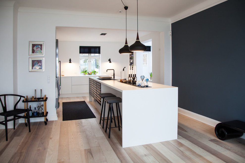 Cette photo montre une cuisine scandinave en L de taille moyenne avec parquet clair, îlot, un sol beige, un plan de travail blanc et un placard à porte plane.