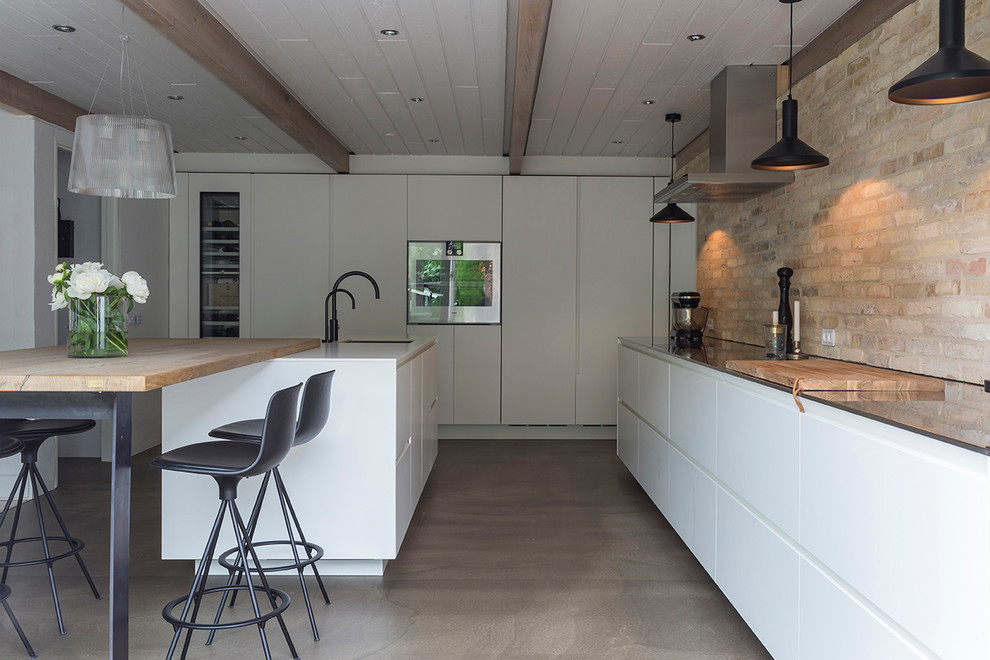 Inredning av ett modernt stort kök, med en undermonterad diskho, släta luckor, vita skåp, bänkskiva i rostfritt stål, betonggolv, en köksö och grått golv