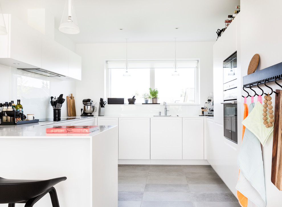 Immagine di una cucina scandinava di medie dimensioni con ante lisce, ante bianche, top in laminato, paraspruzzi bianco, paraspruzzi con lastra di vetro, elettrodomestici neri, pavimento con piastrelle in ceramica e penisola