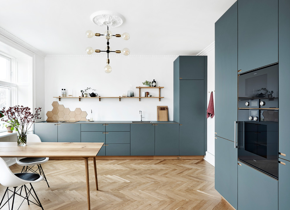 This is an example of a large scandinavian l-shaped kitchen/diner in Copenhagen with flat-panel cabinets, blue cabinets, a single-bowl sink, brown splashback, wood splashback, coloured appliances, light hardwood flooring, no island and beige floors.