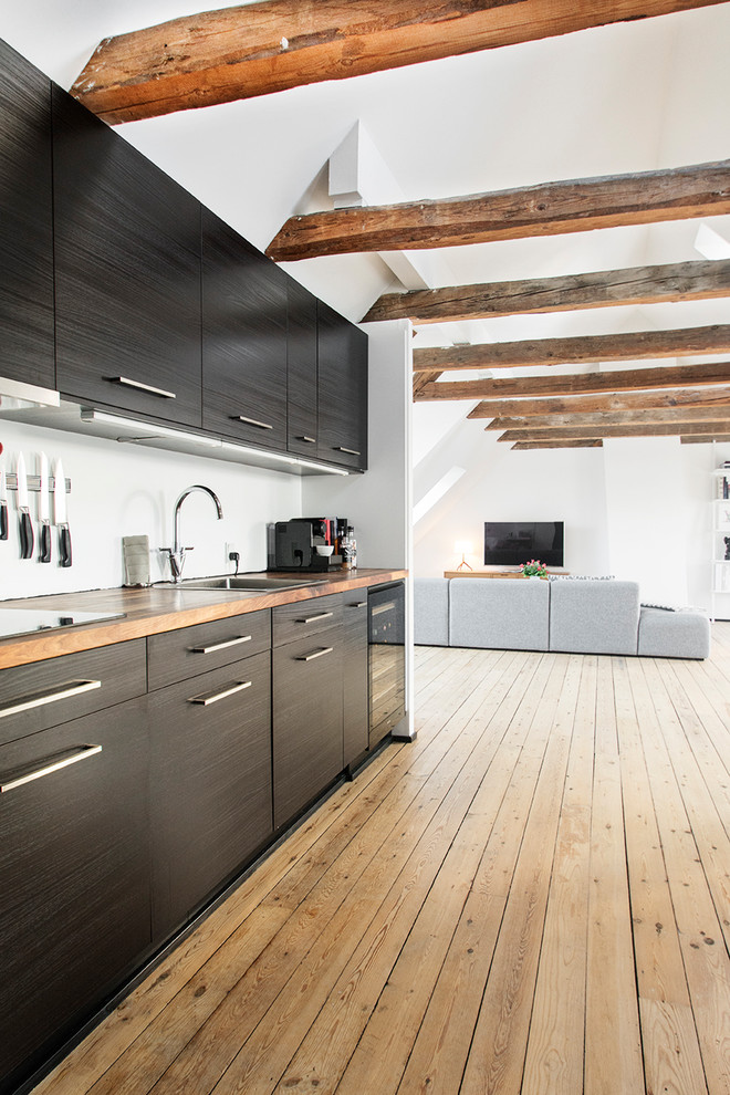 コペンハーゲンにあるコンテンポラリースタイルのおしゃれなキッチン (シングルシンク、フラットパネル扉のキャビネット、黒いキャビネット、木材カウンター、黒い調理設備、無垢フローリング、アイランドなし、ベージュの床) の写真