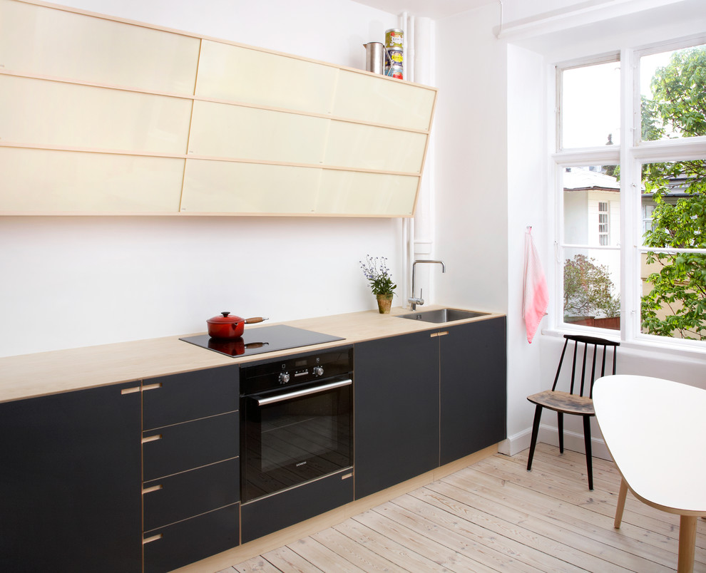 Kleine Nordische Wohnküche in L-Form mit Einbauwaschbecken, flächenbündigen Schrankfronten, schwarzen Schränken, Arbeitsplatte aus Holz, hellem Holzboden und Kücheninsel in Kopenhagen