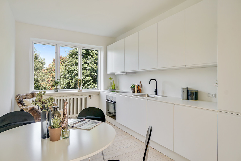 Danish single-wall light wood floor and beige floor eat-in kitchen photo in Copenhagen with a drop-in sink, flat-panel cabinets, white cabinets, white backsplash, paneled appliances, no island and white countertops
