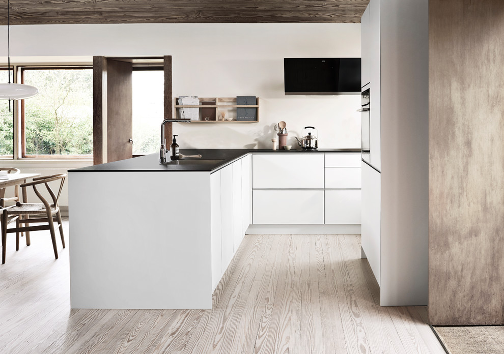 コペンハーゲンにある北欧スタイルのおしゃれなキッチン (アンダーカウンターシンク、フラットパネル扉のキャビネット、白いキャビネット、白いキッチンパネル、淡色無垢フローリング、ベージュの床、黒いキッチンカウンター) の写真