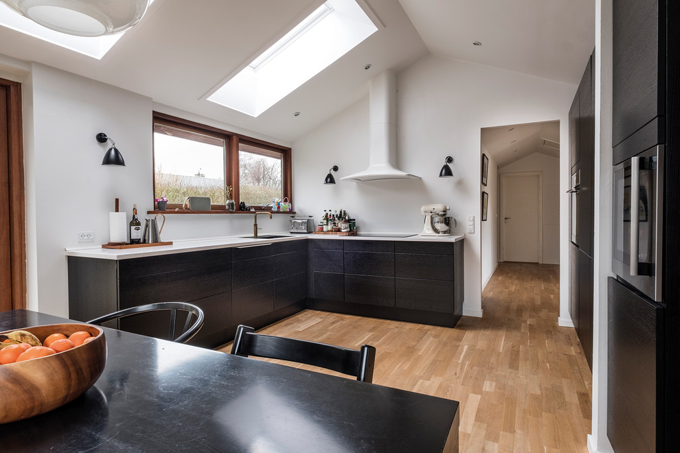 This is an example of a scandinavian u-shaped kitchen/diner in Copenhagen with flat-panel cabinets, black cabinets, white splashback, medium hardwood flooring, a built-in sink, black appliances, no island and beige floors.