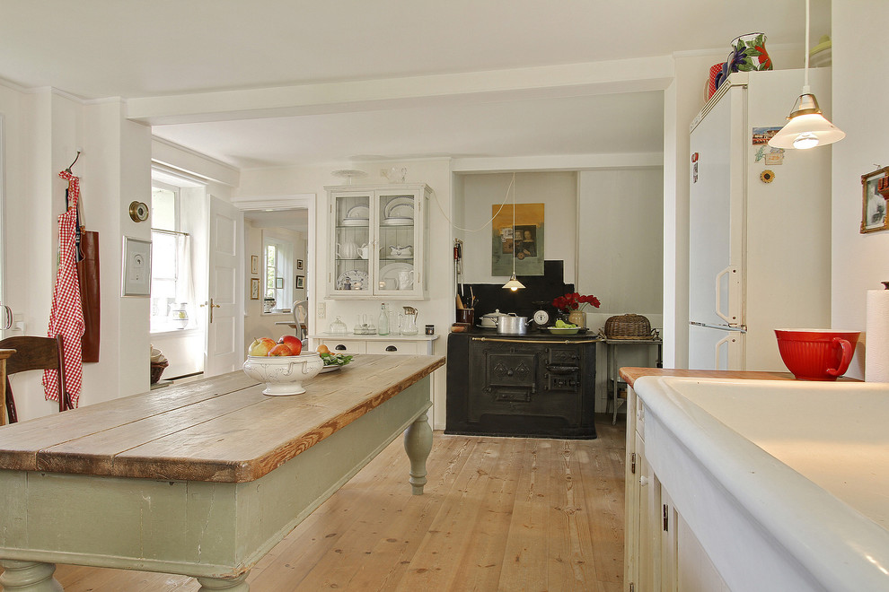 Mittelgroße Country Wohnküche ohne Insel in L-Form mit weißen Schränken, Arbeitsplatte aus Holz, Küchenrückwand in Schwarz, weißen Elektrogeräten und hellem Holzboden in Kopenhagen
