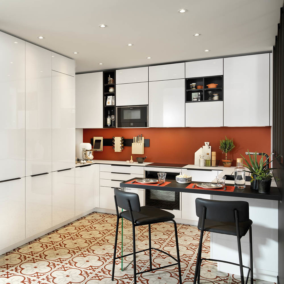 На фото: п-образная кухня в современном стиле с плоскими фасадами, оранжевым фартуком, полуостровом, разноцветным полом, белой столешницей, черно-белыми фасадами и барной стойкой с