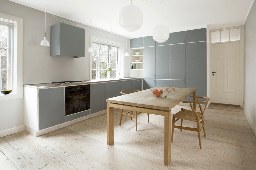 Medium sized scandi l-shaped kitchen/diner in Copenhagen with a built-in sink, recessed-panel cabinets, grey cabinets, stainless steel worktops, black appliances, light hardwood flooring and no island.