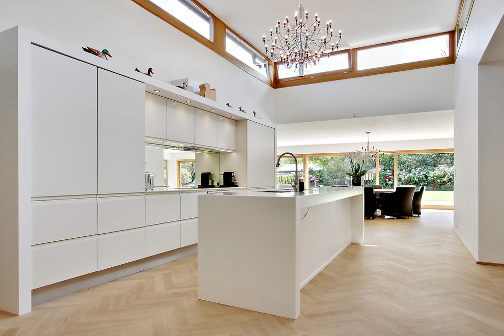 Пример оригинального дизайна: большая параллельная кухня-гостиная в стиле модернизм с одинарной мойкой, плоскими фасадами, белыми фасадами, столешницей из ламината, цветной техникой, светлым паркетным полом и островом