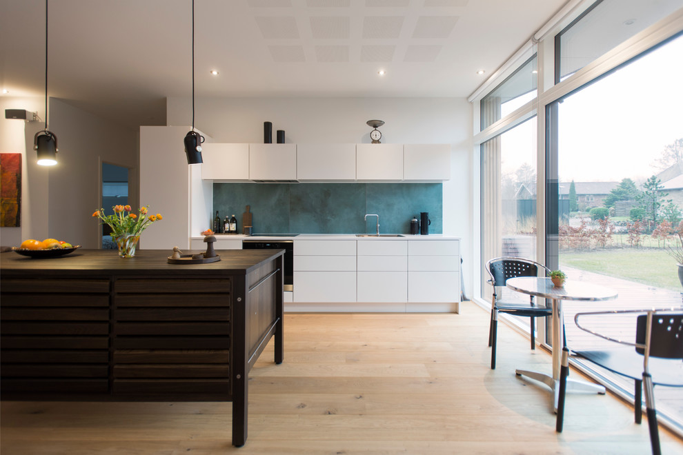Moderne Wohnküche mit weißen Schränken, Küchenrückwand in Blau, hellem Holzboden und Kücheninsel in Aarhus