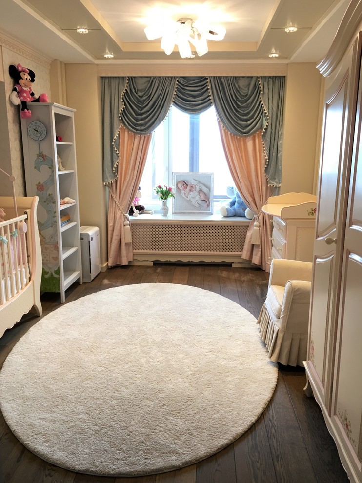 Ejemplo de habitación de bebé niña clásica de tamaño medio con paredes beige y suelo de madera oscura