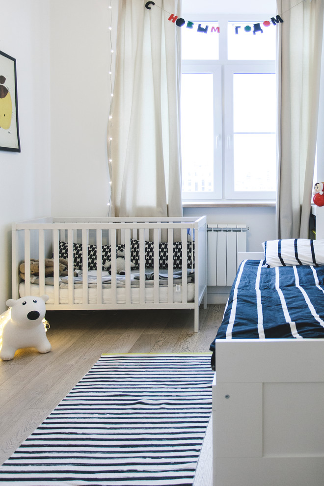 Cette image montre une chambre de bébé garçon nordique avec un mur blanc et un sol en bois brun.