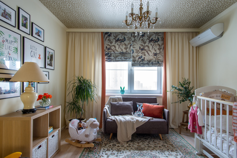 Photo of a traditional nursery for girls in Moscow with beige walls, light hardwood flooring and feature lighting.