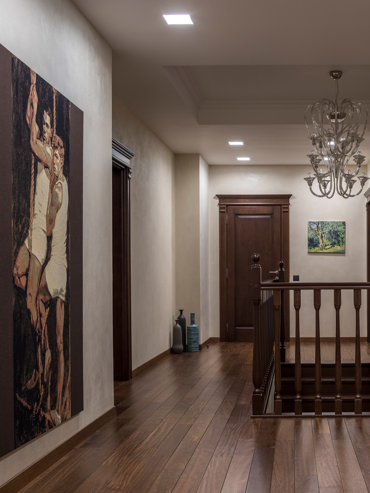 На фото: большой коридор в стиле неоклассика (современная классика) с бежевыми стенами, темным паркетным полом и коричневым полом