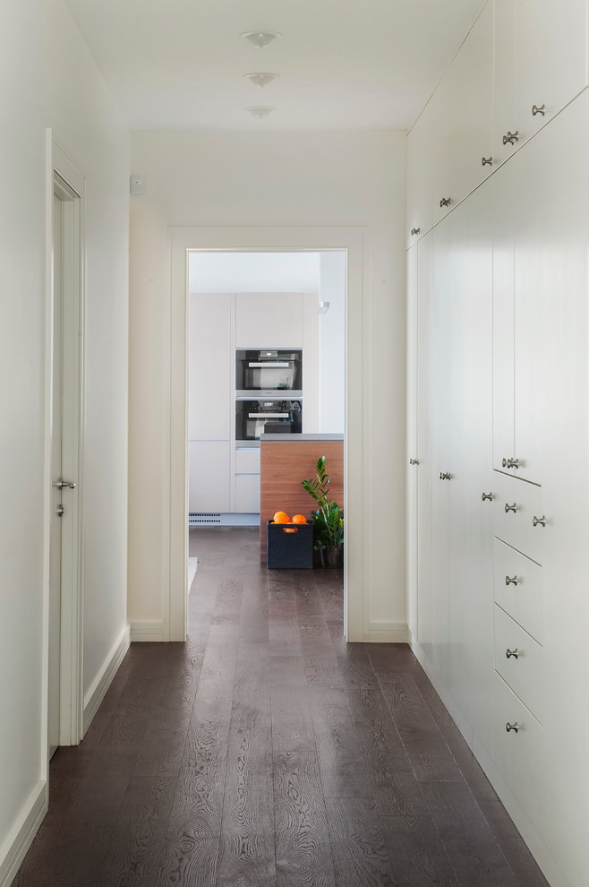 Cette photo montre un couloir tendance avec un mur blanc, parquet foncé et un sol marron.