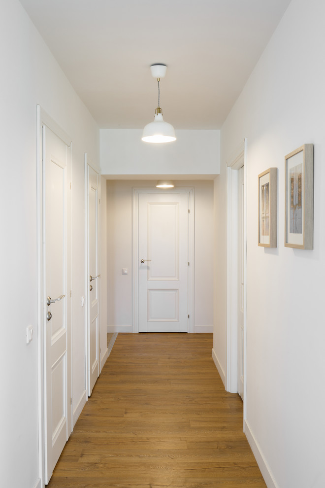 Cette image montre un couloir nordique avec un mur blanc et un sol en bois brun.