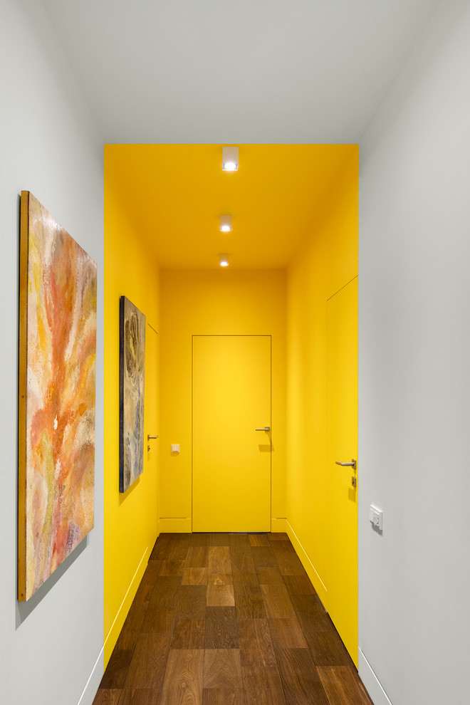Diseño de recibidores y pasillos contemporáneos con paredes amarillas, suelo de madera oscura, suelo marrón y cuadros
