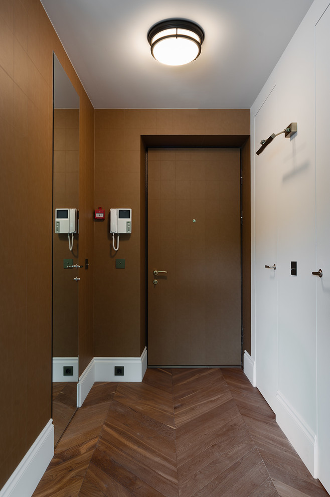 Cette photo montre un petit couloir tendance avec un mur blanc et un sol en bois brun.