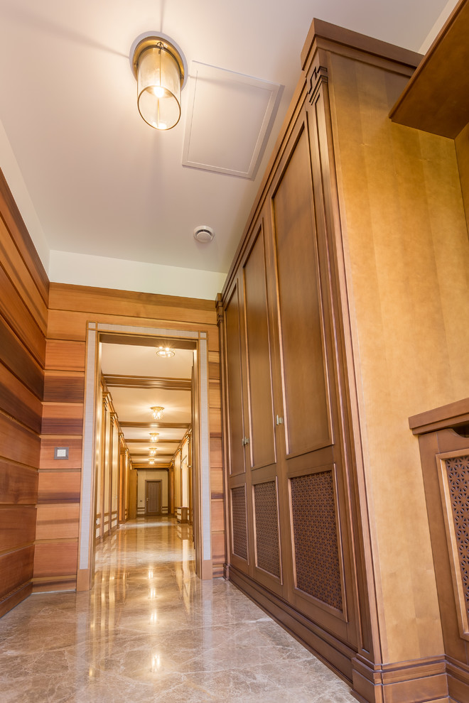На фото: большой коридор в классическом стиле с коричневыми стенами и мраморным полом с