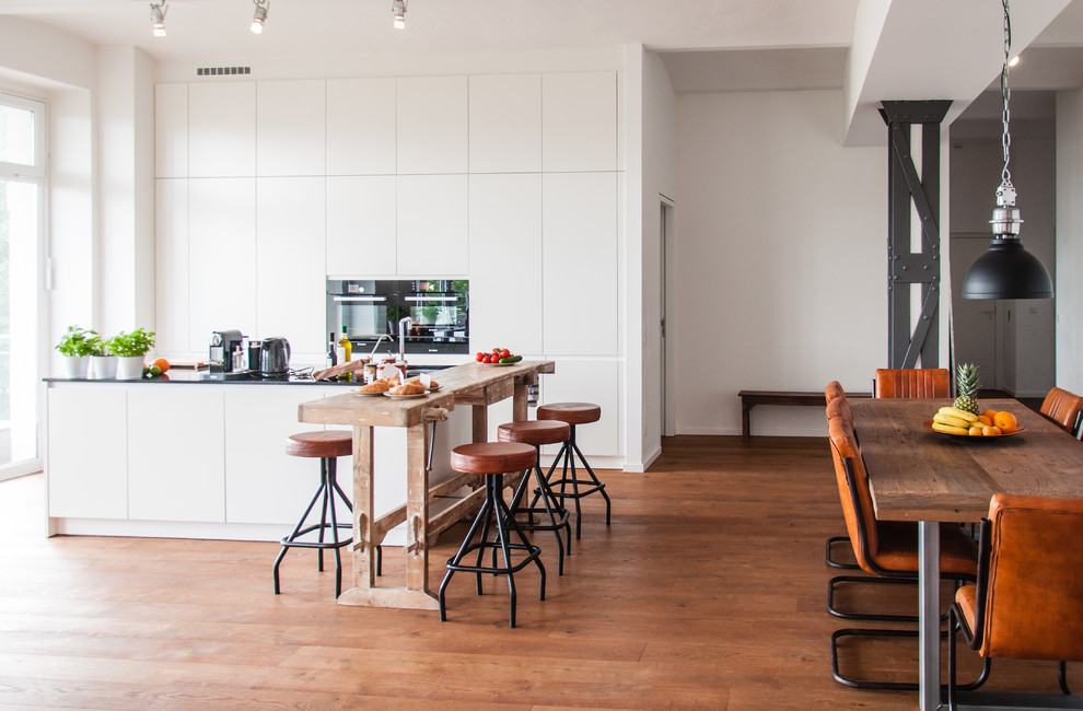Offene, Geräumige Shabby-Style Küche mit weißen Schränken, Granit-Arbeitsplatte und braunem Holzboden in Berlin