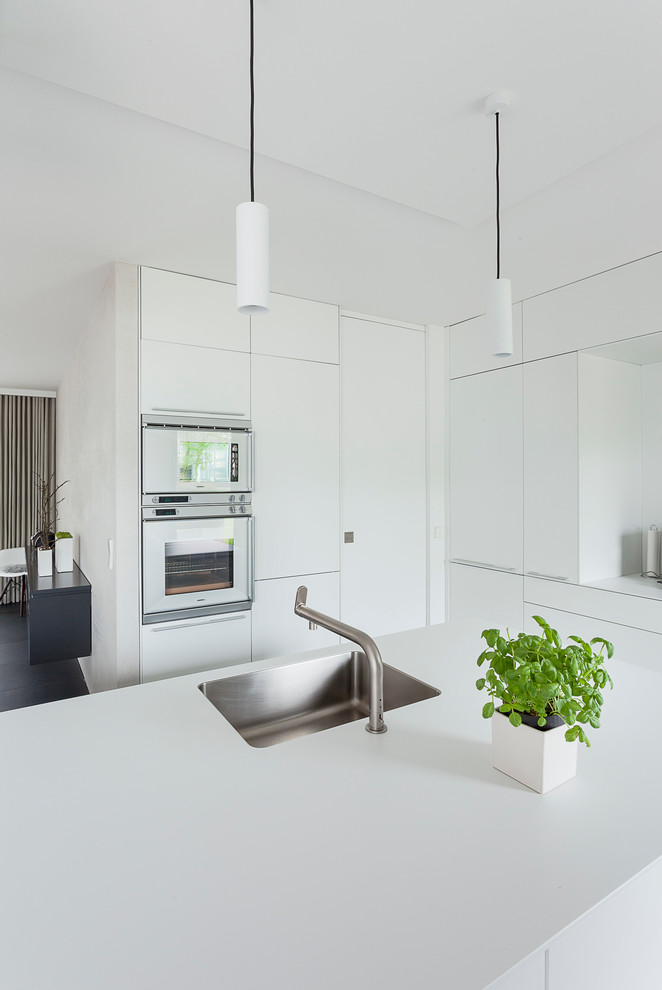 Mittelgroße Moderne Küche mit Unterbauwaschbecken, flächenbündigen Schrankfronten, weißen Schränken, Küchengeräten aus Edelstahl und Kücheninsel in Hannover
