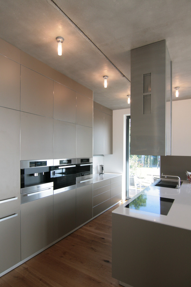 Bild på ett avskilt, mellanstort funkis kök, med en dubbel diskho, släta luckor, grå skåp, integrerade vitvaror, mellanmörkt trägolv och en köksö