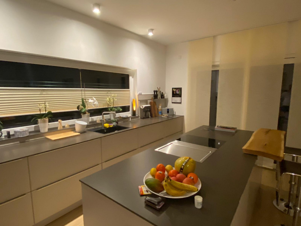 На фото: кухня-гостиная среднего размера в современном стиле с одинарной мойкой, плоскими фасадами, серыми фасадами, черной техникой, островом и столешницей из кварцевого агломерата с