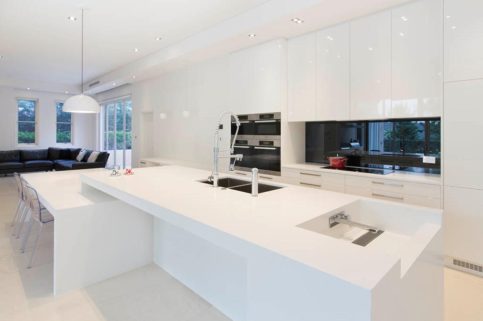Foto på ett stort funkis linjärt kök och matrum, med en dubbel diskho, släta luckor, vita skåp, svart stänkskydd, rostfria vitvaror och en köksö