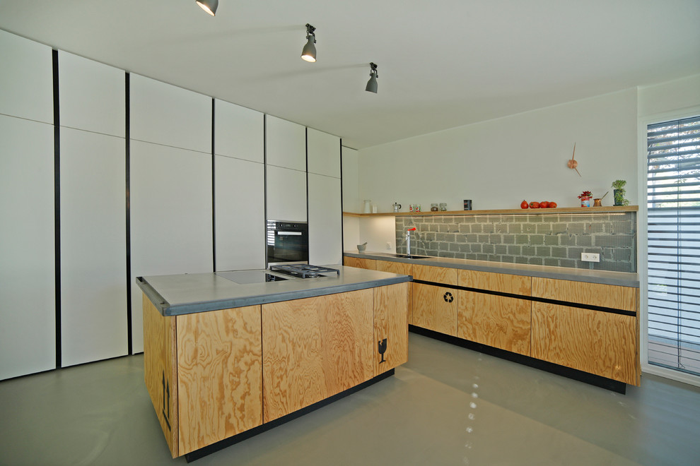 This is an example of a large industrial single-wall kitchen/diner in Munich with an integrated sink, flat-panel cabinets, medium wood cabinets, composite countertops, grey splashback, glass sheet splashback, stainless steel appliances, concrete flooring and an island.
