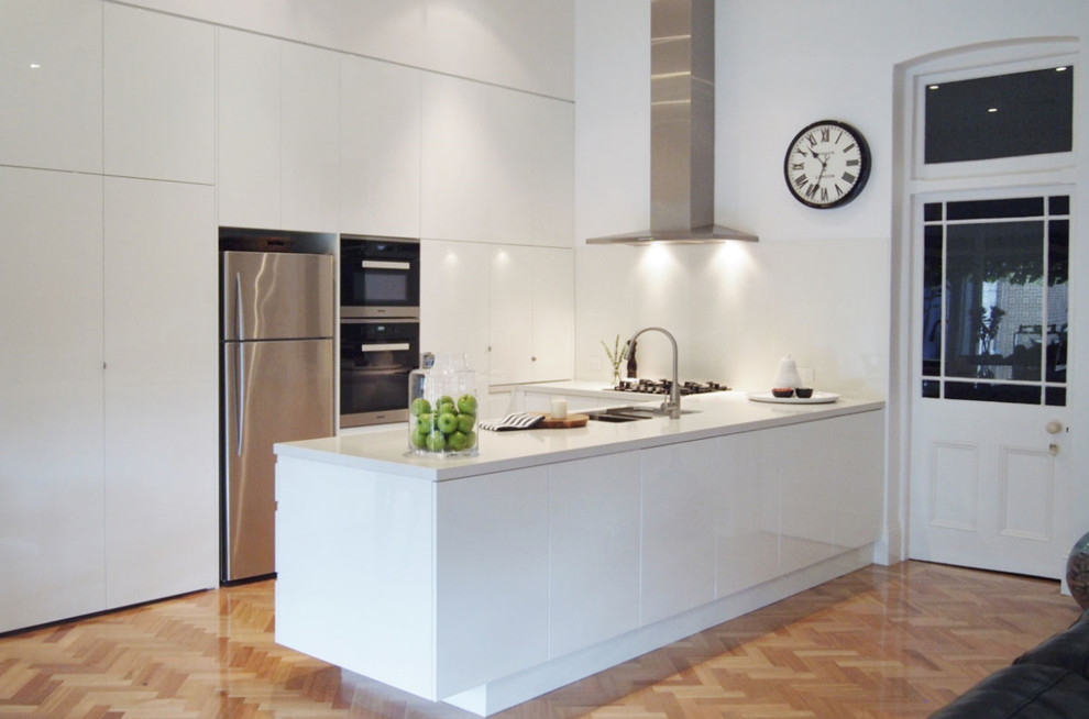 На фото: угловая кухня среднего размера в современном стиле с накладной мойкой, плоскими фасадами, белыми фасадами и паркетным полом среднего тона