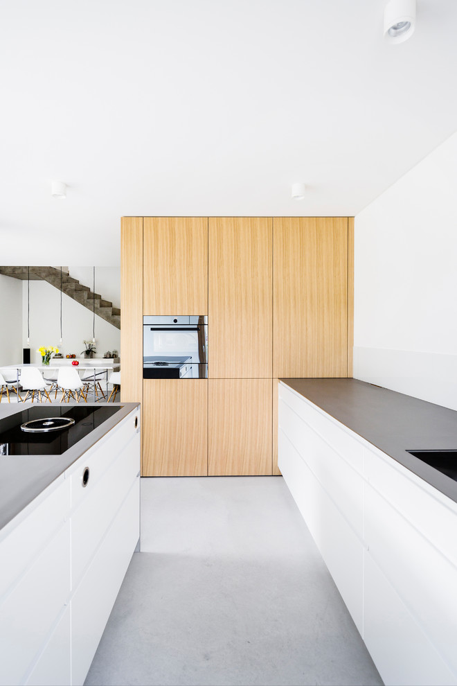 Idéer för att renovera ett mellanstort funkis linjärt kök med öppen planlösning, med en integrerad diskho, släta luckor, vita skåp, bänkskiva i rostfritt stål, vitt stänkskydd, glaspanel som stänkskydd, svarta vitvaror, betonggolv, en köksö och grått golv