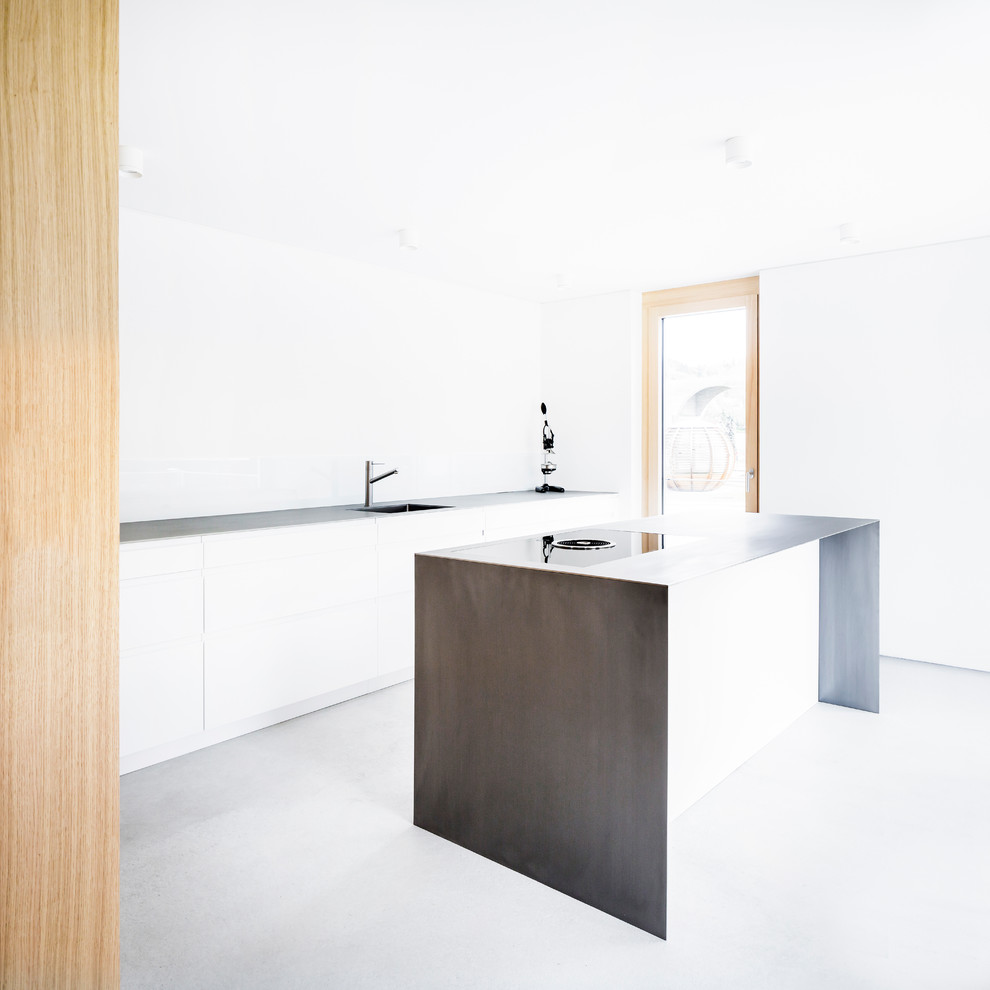 Idéer för att renovera ett mellanstort funkis linjärt kök med öppen planlösning, med en integrerad diskho, släta luckor, vita skåp, bänkskiva i rostfritt stål, vitt stänkskydd, glaspanel som stänkskydd, svarta vitvaror, betonggolv, en köksö och grått golv