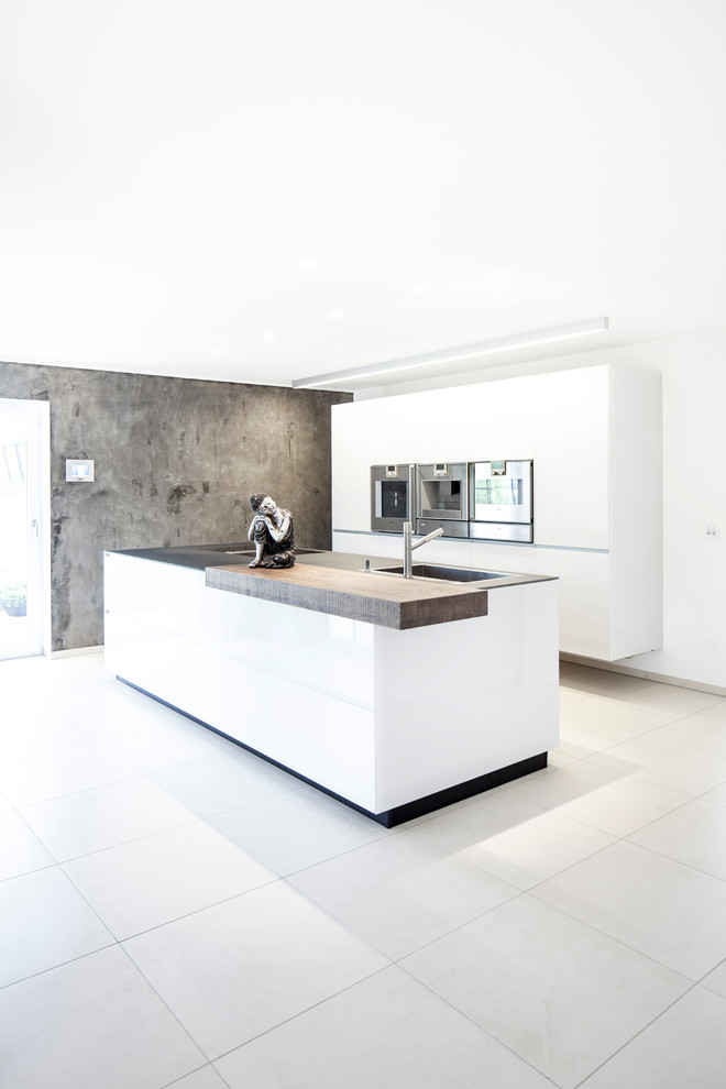 Offene Moderne Küche mit Einbauwaschbecken, flächenbündigen Schrankfronten, weißen Schränken, Küchengeräten aus Edelstahl, Betonboden und Kücheninsel in Stuttgart