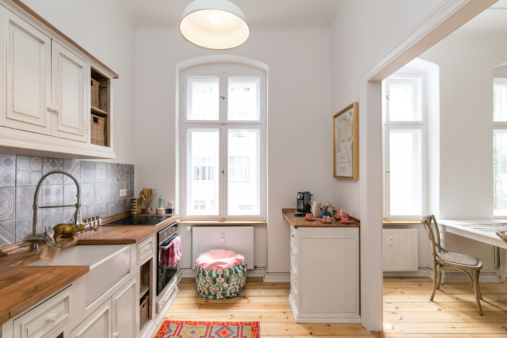 Scandinavian single-wall kitchen in Berlin with a belfast sink, raised-panel cabinets, white cabinets, wood worktops, multi-coloured splashback, light hardwood flooring, no island and beige floors.