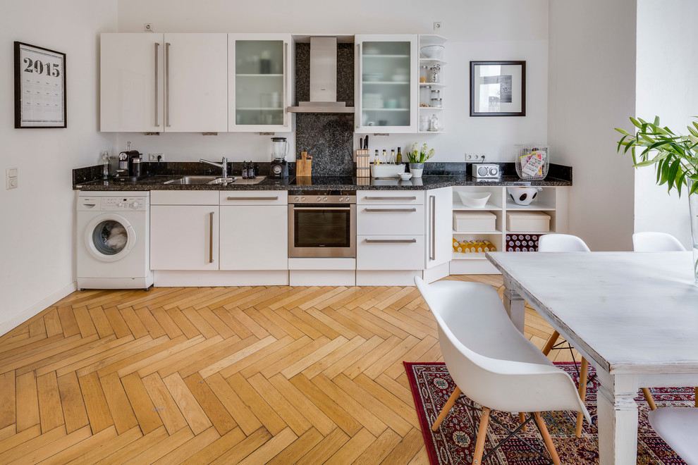 Foto på ett stort nordiskt linjärt kök och matrum, med släta luckor, vita skåp, ljust trägolv, en nedsänkt diskho, granitbänkskiva, grått stänkskydd, stänkskydd i stenkakel och rostfria vitvaror