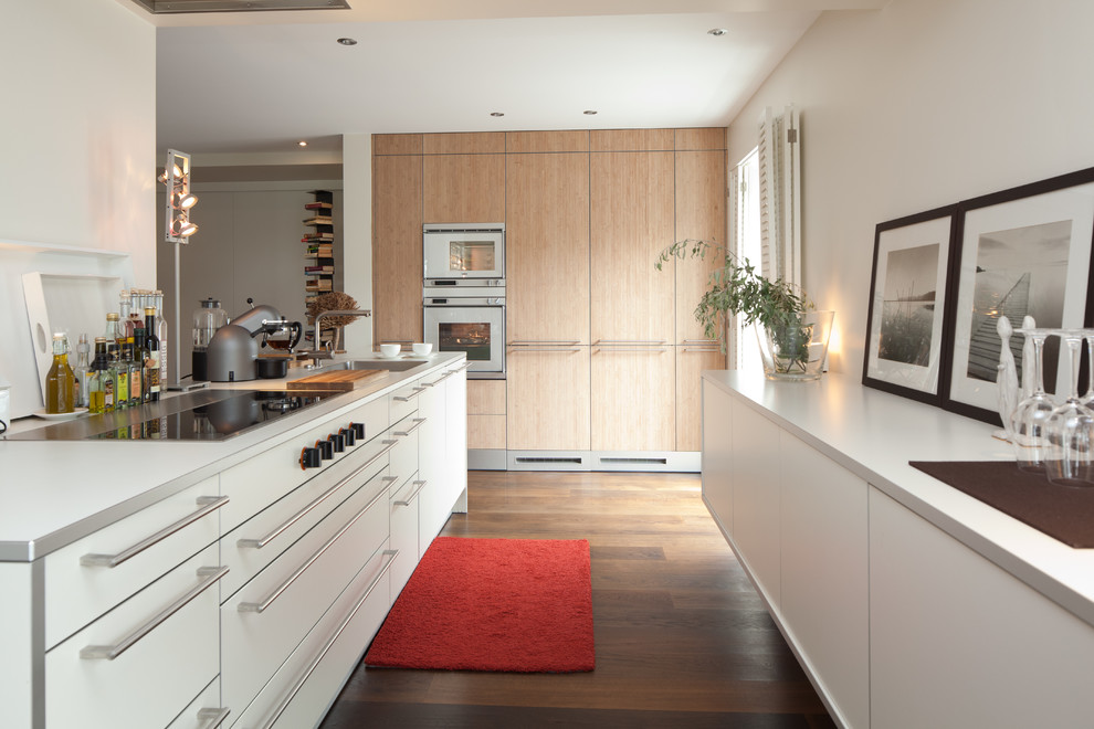 Exempel på ett stort modernt kök med öppen planlösning, med en nedsänkt diskho, släta luckor, vita skåp, vitt stänkskydd, mörkt trägolv och integrerade vitvaror