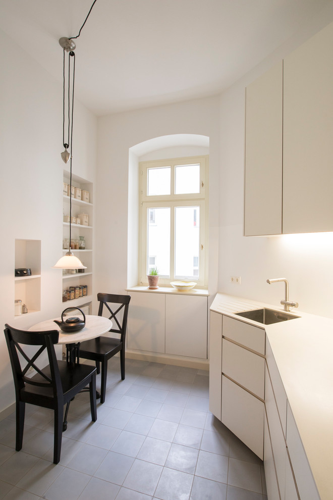 Immagine di una piccola cucina lineare minimal chiusa con lavello da incasso, ante lisce, ante bianche, paraspruzzi bianco, nessuna isola, pavimento grigio e top bianco