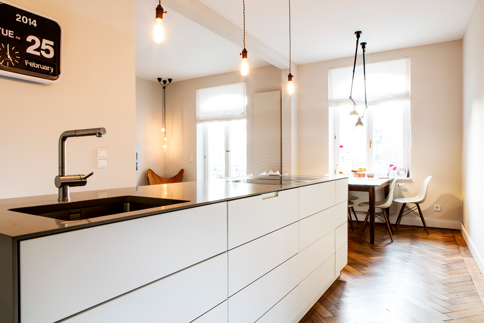 Medium sized contemporary single-wall open plan kitchen in Munich with an integrated sink, flat-panel cabinets, white cabinets, composite countertops, white splashback, limestone splashback, stainless steel appliances, medium hardwood flooring, an island and brown floors.