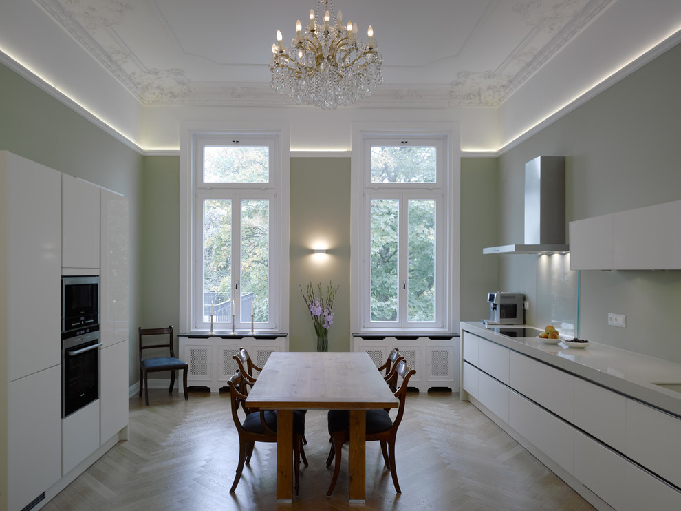 ハンブルクにある広いコンテンポラリースタイルのおしゃれなキッチン (フラットパネル扉のキャビネット、白いキャビネット、緑のキッチンパネル、ガラス板のキッチンパネル、黒い調理設備、無垢フローリング) の写真