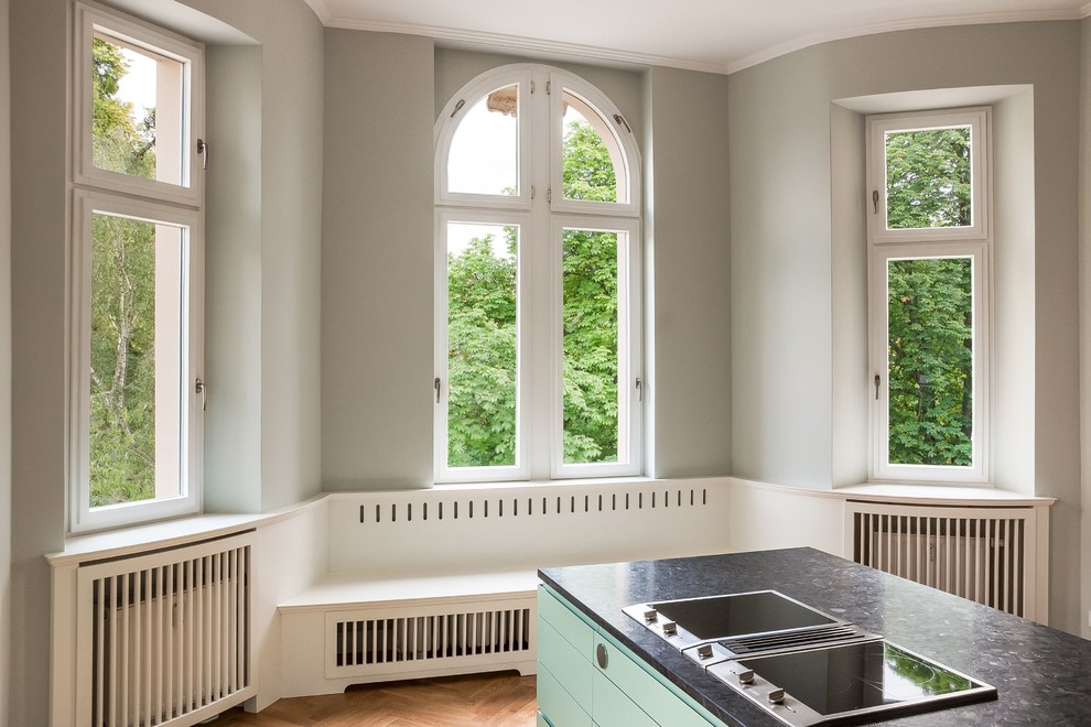 Photo of a large traditional l-shaped kitchen/diner in Berlin with a submerged sink, flat-panel cabinets, green cabinets, granite worktops, white splashback, porcelain splashback, stainless steel appliances, medium hardwood flooring, an island, brown floors and black worktops.