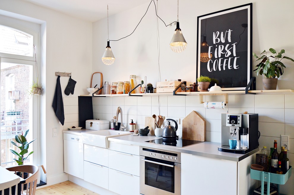 デュッセルドルフにある小さな北欧スタイルのおしゃれなキッチン (エプロンフロントシンク、フラットパネル扉のキャビネット、シルバーの調理設備、淡色無垢フローリング、アイランドなし、ステンレスカウンター、白いキッチンパネル、セラミックタイルのキッチンパネル) の写真
