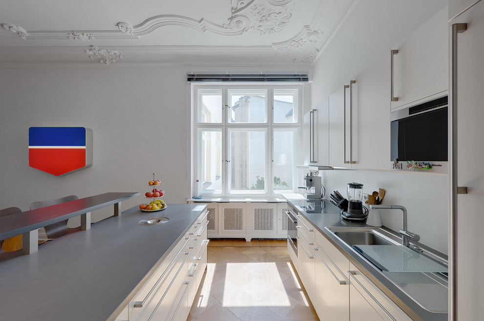 This is an example of a medium sized contemporary single-wall open plan kitchen in Berlin with flat-panel cabinets, a built-in sink, white cabinets, integrated appliances, white splashback and an island.