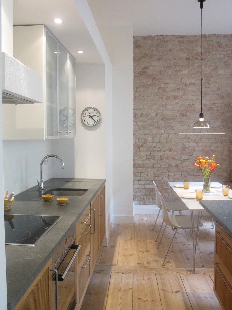 Moderne Wohnküche mit hellbraunen Holzschränken, Kalkstein-Arbeitsplatte, Küchengeräten aus Edelstahl, hellem Holzboden, Kücheninsel und Unterbauwaschbecken in Berlin